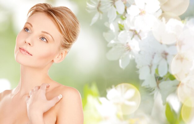 concetto di bellezza, persone e cura del corpo - bel viso di giovane donna e mani sullo sfondo di fiori di ciliegio primaverile naturale