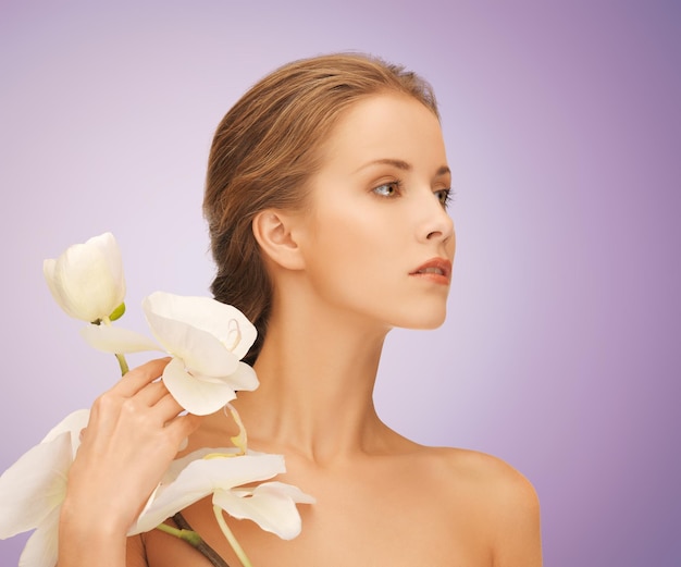 concetto di bellezza, persone e salute - bella giovane donna con fiori di orchidea e spalle nude su sfondo viola