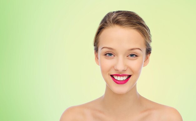 concetto di bellezza, persone e salute - volto sorridente di giovane donna con rossetto rosa su labbra e spalle su sfondo verde naturale