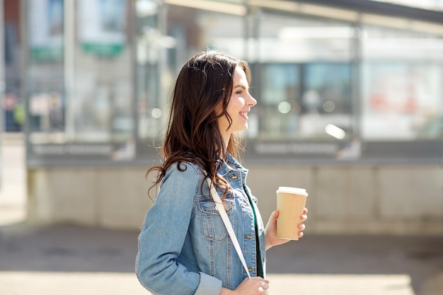 concetto di bevande e persone - giovane donna felice o adolescente che beve caffè dalla tazza di carta sulla strada della città