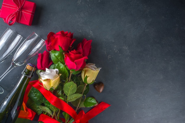 Concetto di biglietto di auguri di San Valentino con fiori di rosa rossa, champagne, cioccolatini e confezione regalo.