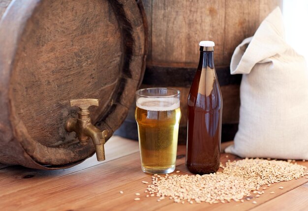 concetto di birreria, bevande e alcolici - primo piano del vecchio barile di birra, vetro, bottiglia e borsa con malto su tavolo di legno