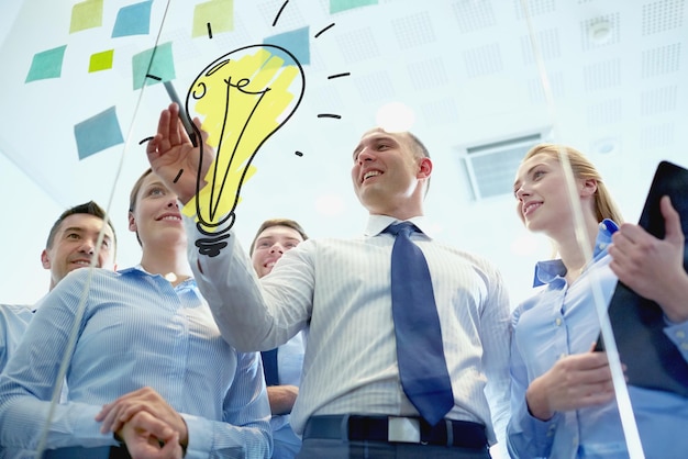 concetto di business, persone, lavoro di squadra e pianificazione - team di lavoro sorridente con pennarello, adesivi e doodle lampadina che lavora in ufficio