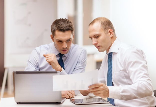 concetto di business, tecnologia e ufficio - due uomini d'affari con laptop, computer tablet pc e documenti che discutono in ufficio