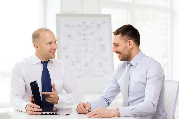 concetto di business, tecnologia e ufficio - due uomini d'affari sorridenti con laptop che hanno presentazione in ufficio