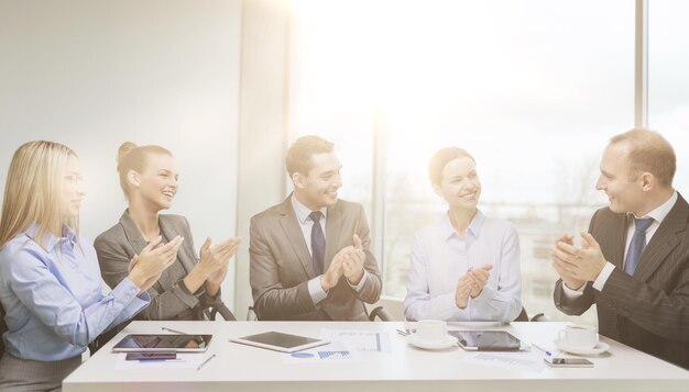 concetto di business, tecnologia e ufficio - team aziendale felice con computer portatili, documenti e caffè che applaudono la mano