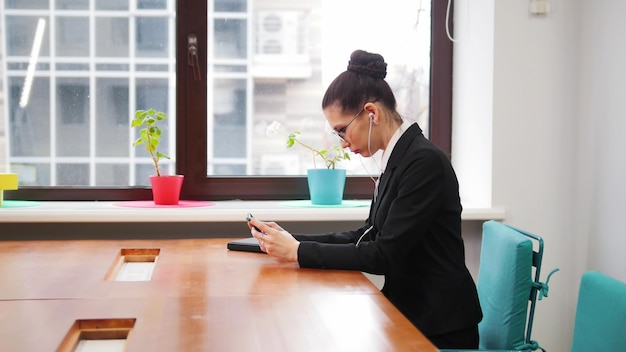 Concetto di business Una donna con gli occhiali si siede vicino al tavolo e inserisce le cuffie nelle orecchie