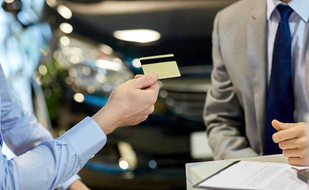 concetto di business, vendita e persone di auto - primo piano del cliente che dà carta di credito al concessionario di auto in auto show o salone