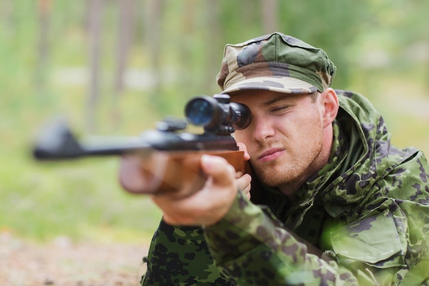 concetto di caccia, guerra, esercito e persone - giovane soldato, ranger o cacciatore con pistola che mira e spara nella foresta