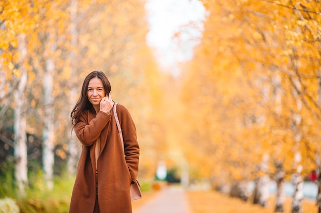 Concetto di caduta - bella donna che beve caffè nella sosta di autunno sotto il fogliame di caduta