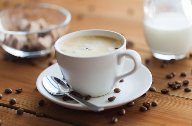 concetto di caffeina, oggetti e bevande - chiuda sulla tazza di caffè e sui grani sulla tavola di legno