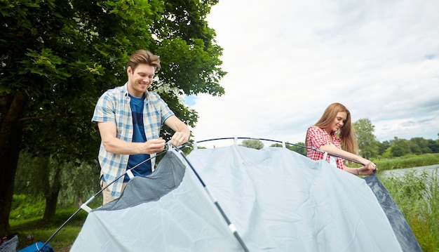 concetto di campeggio, viaggi, turismo, escursione e persone - coppia felice che monta una tenda all'aperto