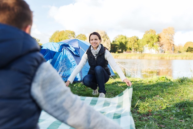 concetto di campeggio, viaggi, turismo, escursione e persone - coppia felice che posa coperta da picnic al campeggio