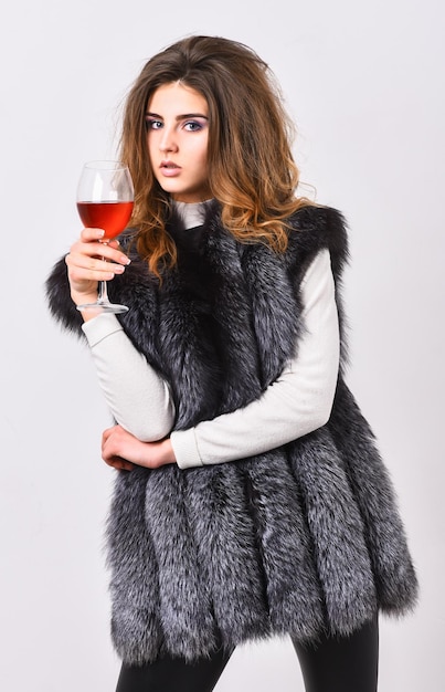 Concetto di cantina di lusso Modello di moda capelli lunghi cappotto di pelliccia o gilet tenere bicchiere di vino La signora alla moda ama il lusso La ragazza gode degli attributi dello stile di vita di lusso Donna bere vino indossare abiti di pelliccia di lusso