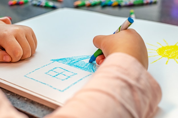 Concetto di casa da sogno. Il bambino disegna una casa con matite colorate su carta. Sogni di casa sua