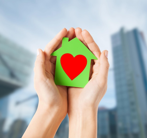concetto di casa di beneficenza, immobiliare e famiglia - foto del primo piano delle mani femminili che tengono la casa di carta verde con cuore rosso