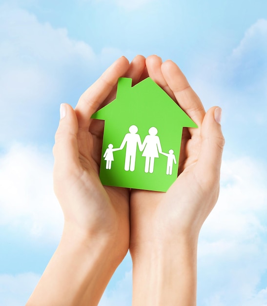 concetto di casa di famiglia e immobiliare - foto del primo piano delle mani femminili che tengono la casa di carta verde con la famiglia