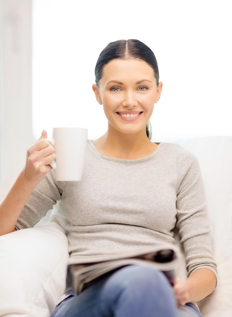 concetto di casa e leasure - donna sorridente con una tazza di caffè o tè che legge una rivista a casa