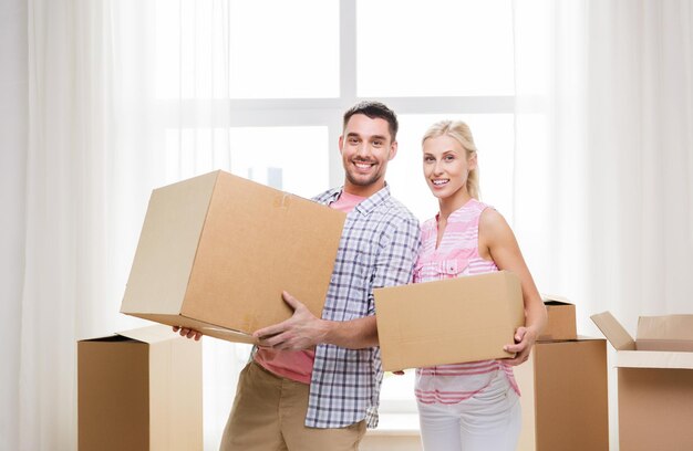 concetto di casa, persone, riparazioni e immobili - coppia sorridente con grandi scatole di cartone che si spostano in un nuovo posto