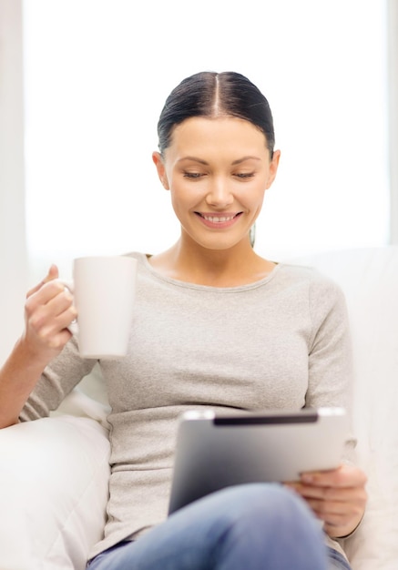 concetto di casa, tecnologia e internet - donna seduta sul divano con tablet pc e tazza a casa
