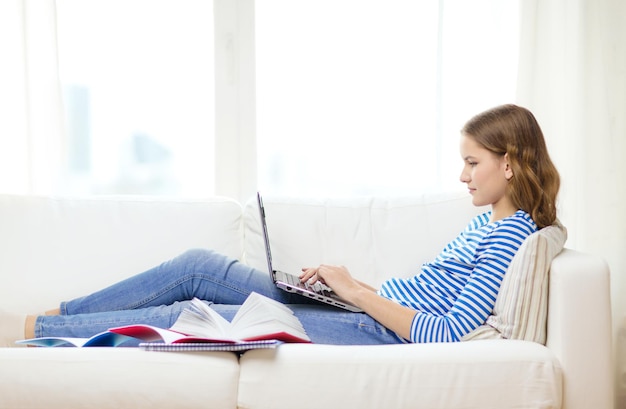 concetto di casa, tecnologia e internet - ragazza impegnata sdraiata sul divano con un computer portatile a casa