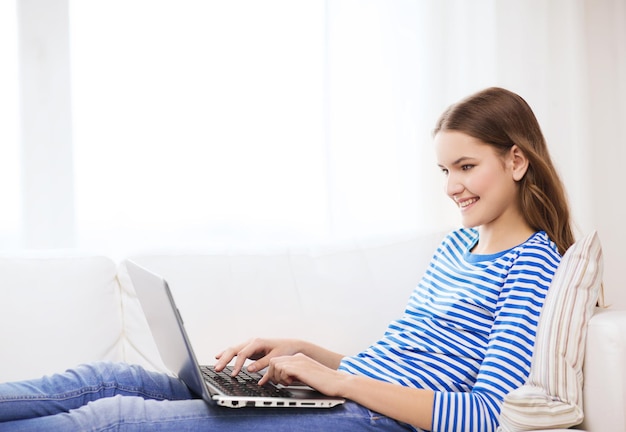 concetto di casa, tecnologia e internet - sorridente ragazza sdraiata sul divano con un computer portatile a casa