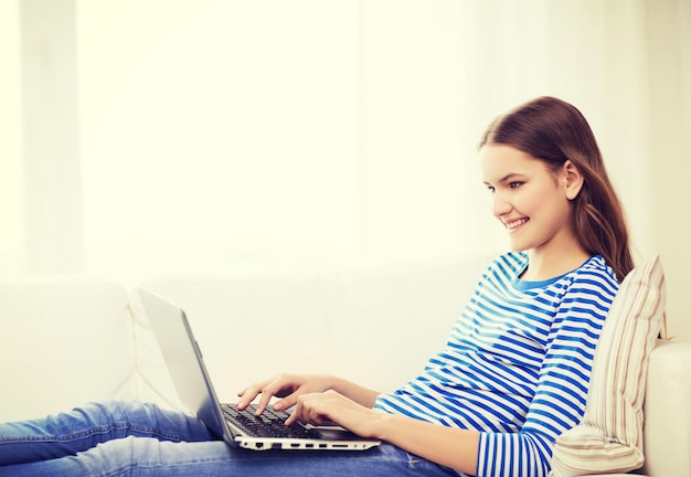 concetto di casa, tecnologia e internet - sorridente ragazza sdraiata sul divano con un computer portatile a casa