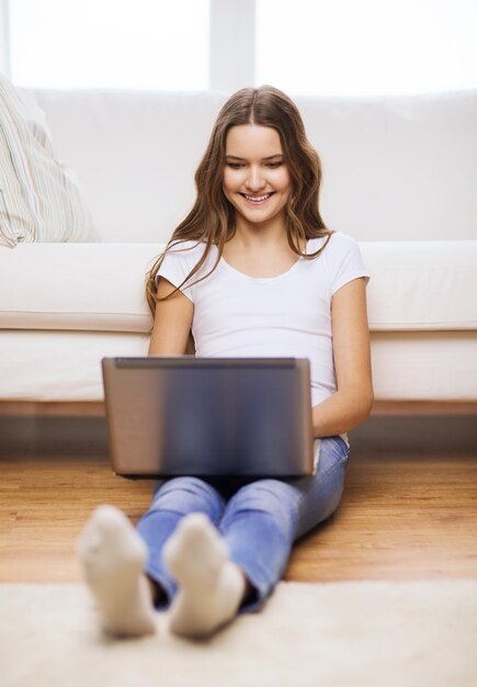 concetto di casa, tecnologia e internet - sorridente ragazza seduta sul pavimento con un computer portatile a casa