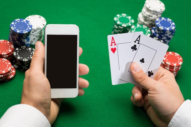 concetto di casinò, gioco d'azzardo online, tecnologia e persone - primo piano del giocatore di poker con carte da gioco, smartphone e fiches al tavolo del casinò verde