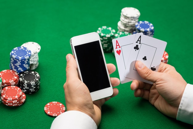 concetto di casinò, gioco d'azzardo online, tecnologia e persone - primo piano del giocatore di poker con carte da gioco, smartphone e fiches al tavolo del casinò verde
