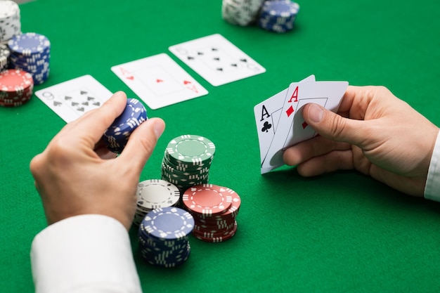 concetto di casinò, gioco d'azzardo, poker, persone e intrattenimento - primo piano del giocatore di poker con carte da gioco e fiches al tavolo del casinò verde