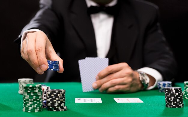 concetto di casinò, gioco d'azzardo, poker, persone e intrattenimento - primo piano del giocatore di poker con carte da gioco e fiches al tavolo del casinò verde