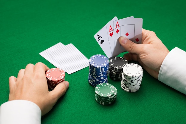 concetto di casinò, gioco d'azzardo, poker, persone e intrattenimento - primo piano del giocatore di poker con carte da gioco e fiches al tavolo del casinò verde