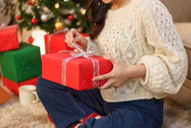 Concetto di celebrazione del Natale Giovane donna asiatica seduta sul pavimento e apertura del regalo di Natale