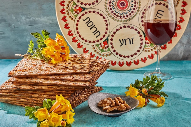 Concetto di celebrazione di Pesach Festa ebraica di Pesach Sfondo con fiori gialli con bicchiere di vino matzah e piatto di seder ai raggi del sole Iscrizioni ebraiche tradizionali su piatto