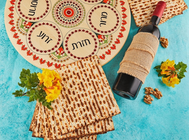 Concetto di celebrazione di Pesach Festa ebraica Pesach Sfondo con fiori gialli con un bicchiere di vino matzah e un piatto di seder su sfondo blu Iscrizioni ebraiche tradizionali su un piatto