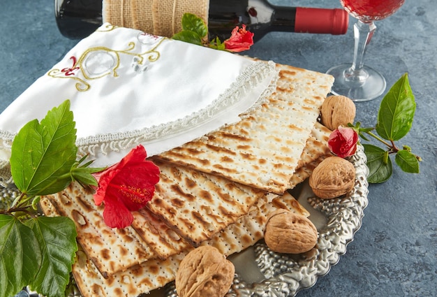 Concetto di celebrazione di Pesach Pasqua ebraica Matzah sulla tradizionale piastra Seder con bottiglia di vino rosso, bicchiere di vino, noci e fiori Close up