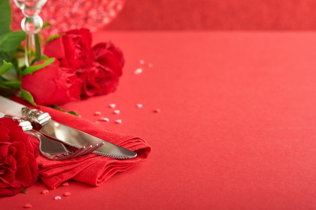 Concetto di cena romantica Tavolo romantico apparecchiare argenteria bicchieri da vino scatola regalo rose e simbolo dell'amore cuore rosso su sfondo rosso San Valentino Matrimonio Compleanno Festa della donna e della mamma