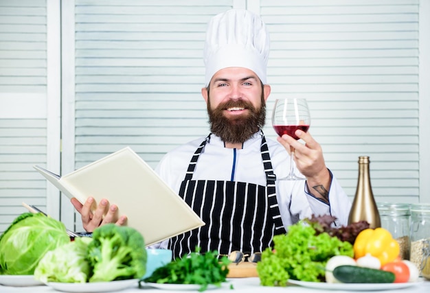 Concetto di cena squisita. Degustazione di vini. Abbina vino e cibo come un esperto. L'uomo indossa un cappello e un grembiule per gustare una bevanda gustosa. Il maestro chef tiene un bicchiere di vino. Aggiungi un po' di alcol. Quale vino accompagnare la cena.