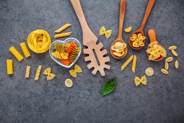 Concetto di cibi italiani e menu design. Vari tipi di pasta su sfondo di pietra scura con piatto posare.