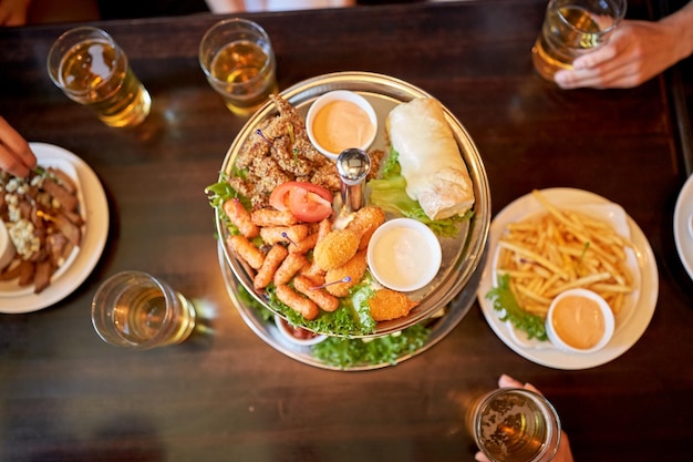 concetto di cibo, bevande e vacanze - tavolo per persone con cibo e bicchieri da birra al bar o al pub
