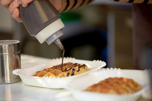 concetto di cibo, cucina, dessert e persone - primo piano del cuoco che aggiunge sciroppo di cioccolato al waffle