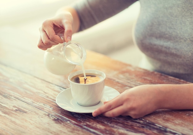 concetto di cibo e casa - primo piano di una donna che versa il latte nel caffè