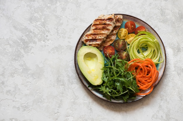 Concetto di cibo equilibrato. Insalata con petto di pollo alla griglia, rucola, avocado, carote e zucchine, mangiare pulito equilibrato, vista dall'alto. Ciotola per il pranzo salutare.