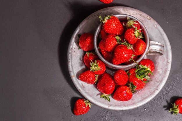 Concetto di cibo estivo con una fragola su uno sfondo di pietra nera. Bacche aromatiche mature, luce dura moderna, ombra scura, vista dall'alto