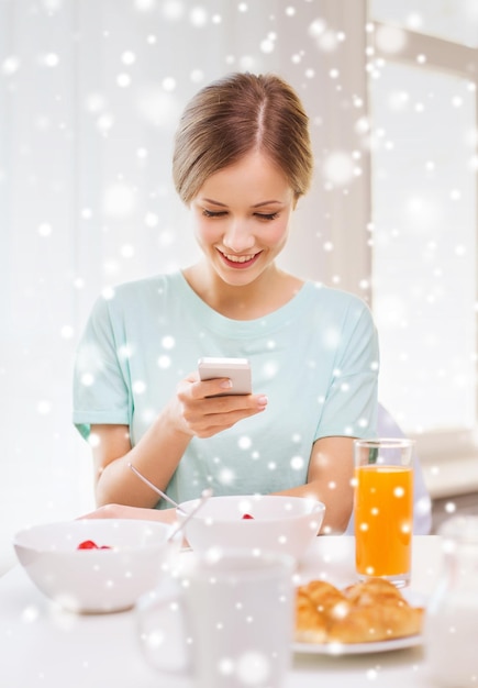 concetto di cibo, persone e tecnologia - donna sorridente con smartphone e fare colazione a casa