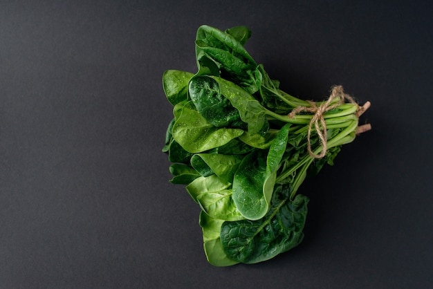 Concetto di cibo pulito. Mazzo di foglie di spinaci biologici freschi su uno sfondo nero. Sana dieta disintossicante primavera-estate. Cibo crudo vegano. Copia spazio.