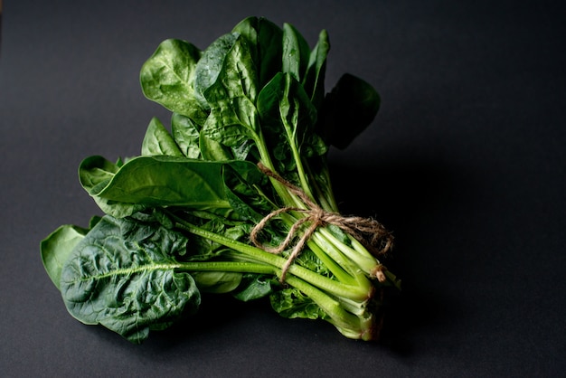 Concetto di cibo pulito. Mazzo di foglie di spinaci biologici freschi su uno sfondo nero. Sana dieta disintossicante primavera-estate. Cibo crudo vegano.