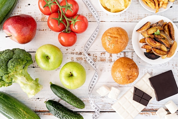 Concetto di cibo sano e malsano. La frutta e la verdura contro i dolci e le patate fritte piano di vista superiore mettono sulla tavola di legno