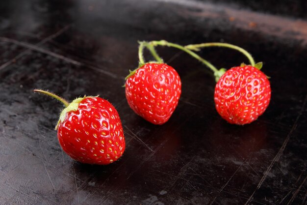 Concetto di cibo sano Fragole rosse succose e dolci con ramoscelli su sfondo nero Primo piano di bacche rosse